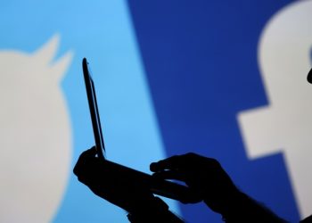 A man is silhouetted against a video screen with a Twitter and a Facebook logo as he poses with an Dell laptop in this photo illustration taken in the central Bosnian town of Zenica, August 14, 2013. REUTERS/Dado Ruvic (BOSNIA AND HERZEGOVINA - Tags: BUSINESS TELECOMS) - RTX12L7W